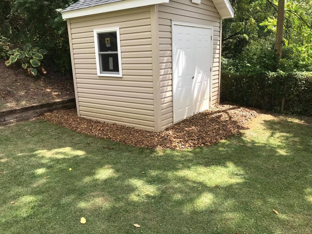 Garden shed with beige siding, white doors, and decorative gravel landscaping.