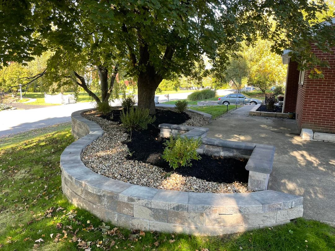 Landscaped garden area with a stone retaining wall and lush greenery by a brick house.