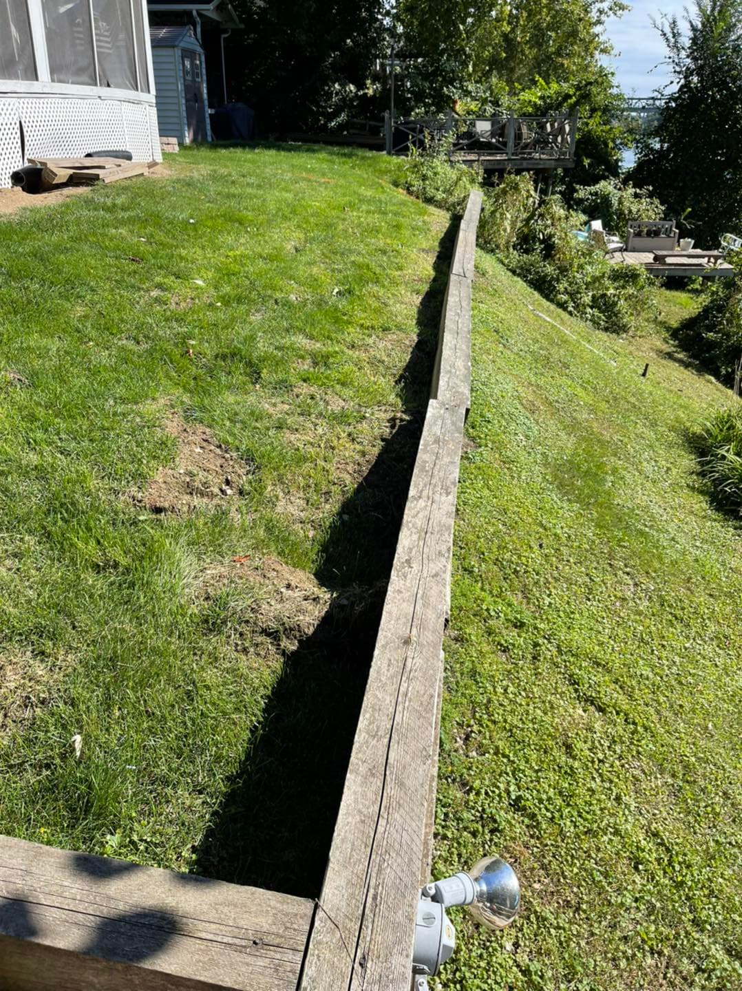 Wooden landscape border along a sloped grassy area with trees and outdoor seating visible.