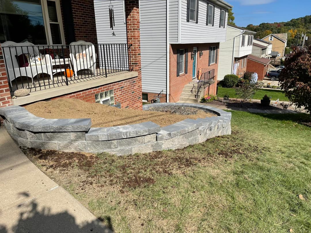 Landscaped yard with a stone retaining wall and sandy area near suburban home.