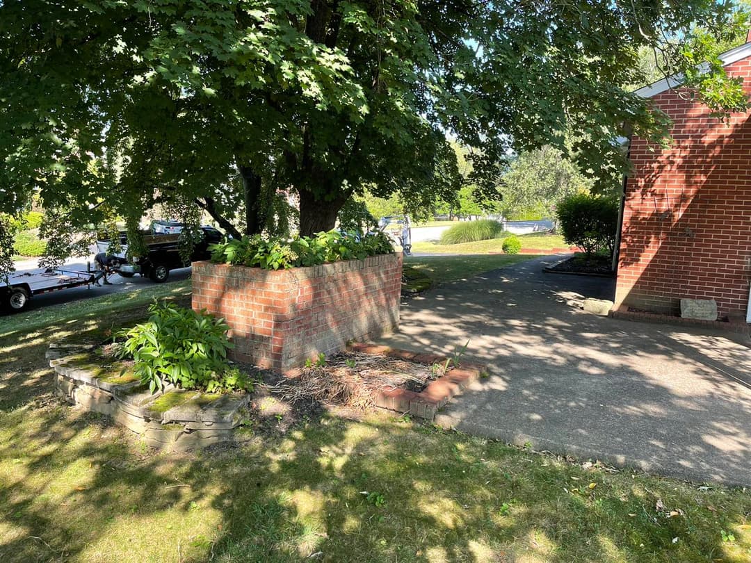 Brick planter and shaded patio area in a residential garden with a visible driveway.