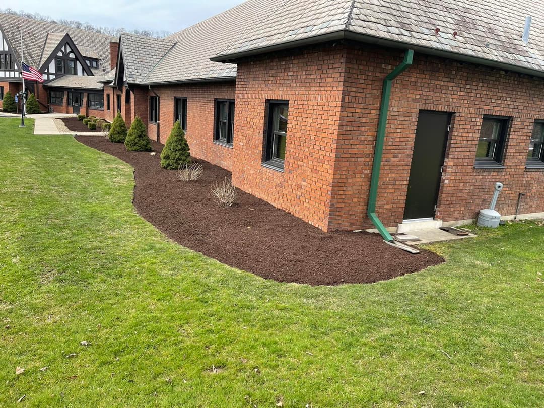 Mulched landscaping around brick building with green grass and hedges in clear weather.