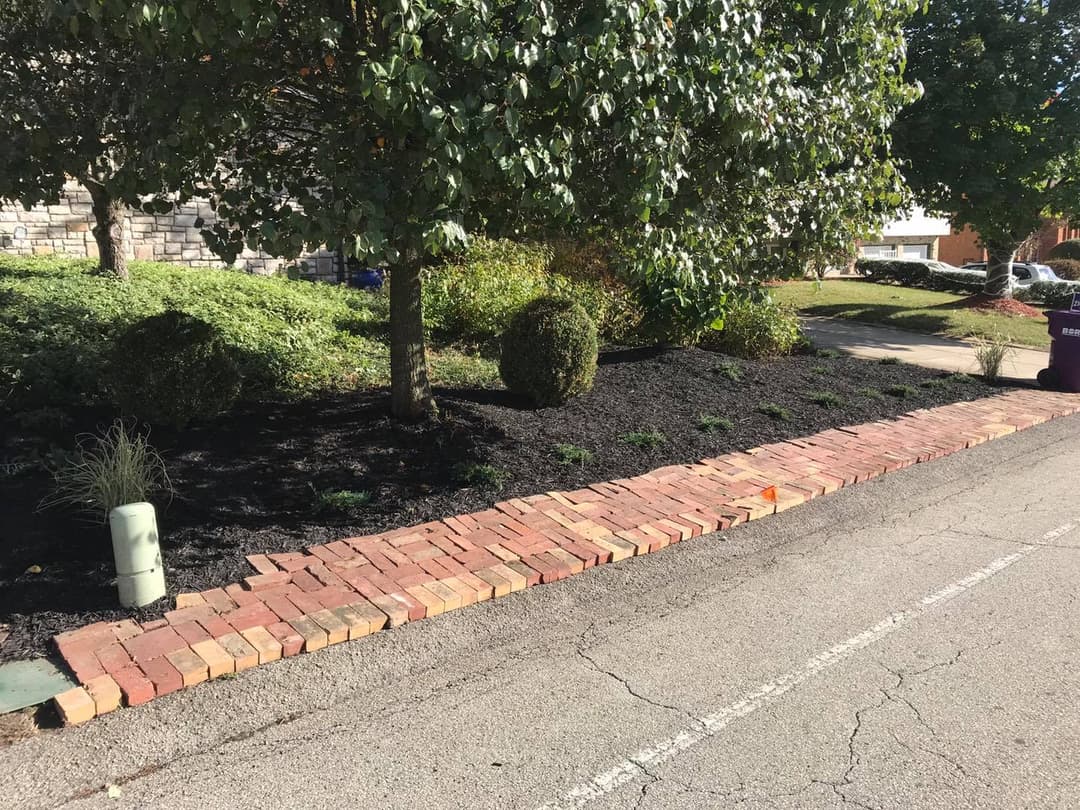 Brick landscaping border with shrubs and mulch along a residential driveway.