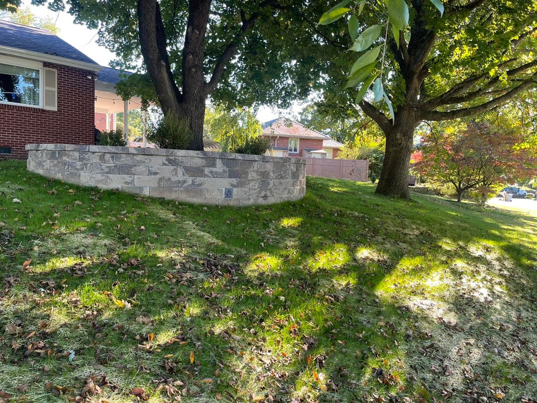 Stone retaining wall in a landscaped yard with trees and a sunny autumn backdrop.