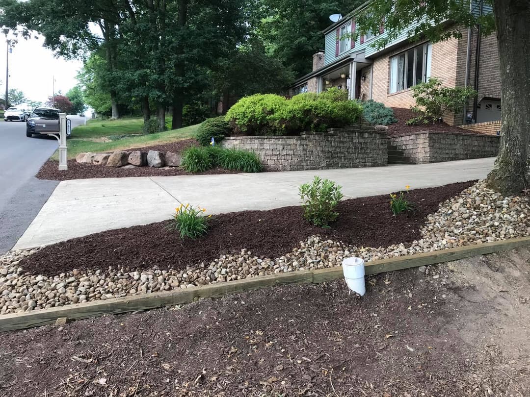 Landscaped front yard with mulch, flowers, and stone border near a residential driveway.