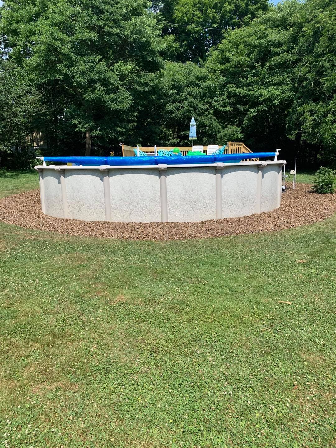 Round above-ground swimming pool surrounded by mulch in a lush green backyard.
