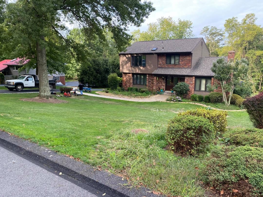 Two-story brown house with green lawn, trees, and parked white pickup truck.