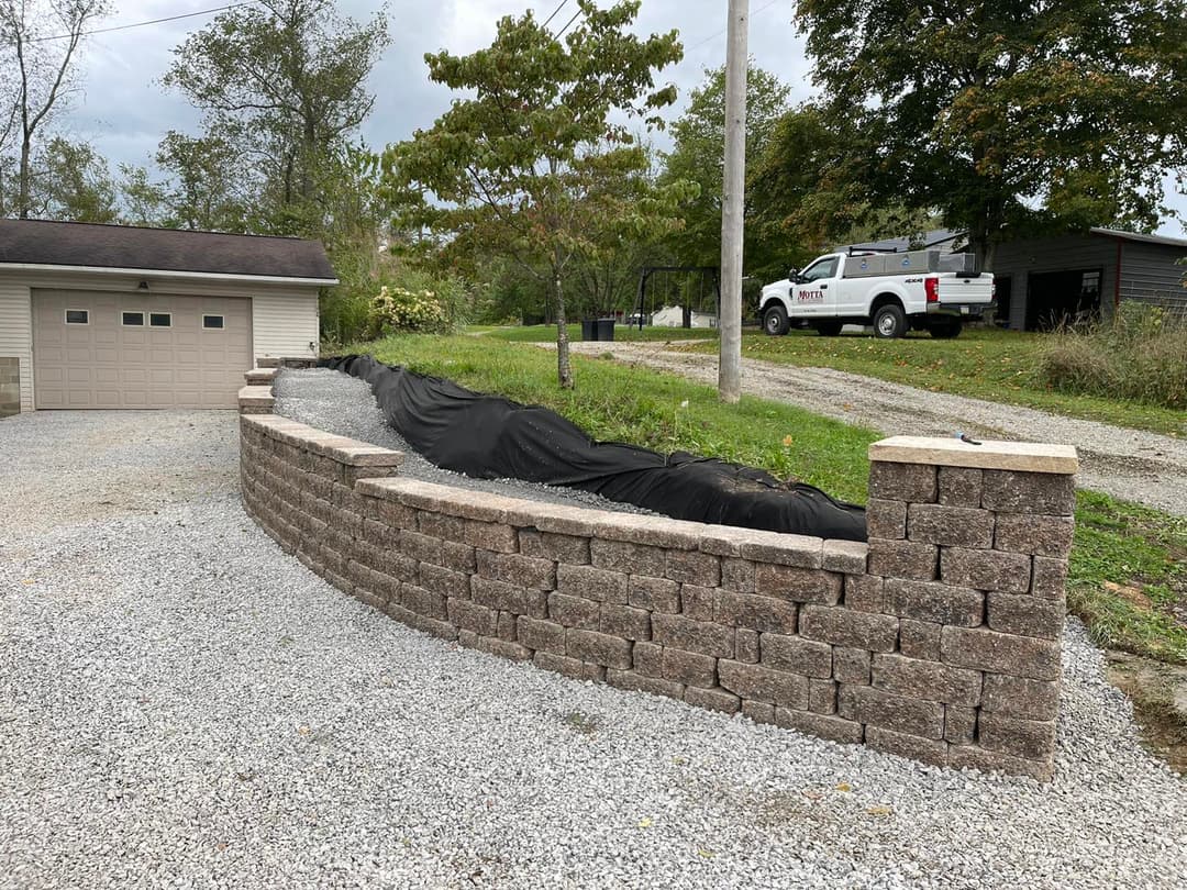 Curved stone retaining wall with gravel and landscaping near a driveway and garage.