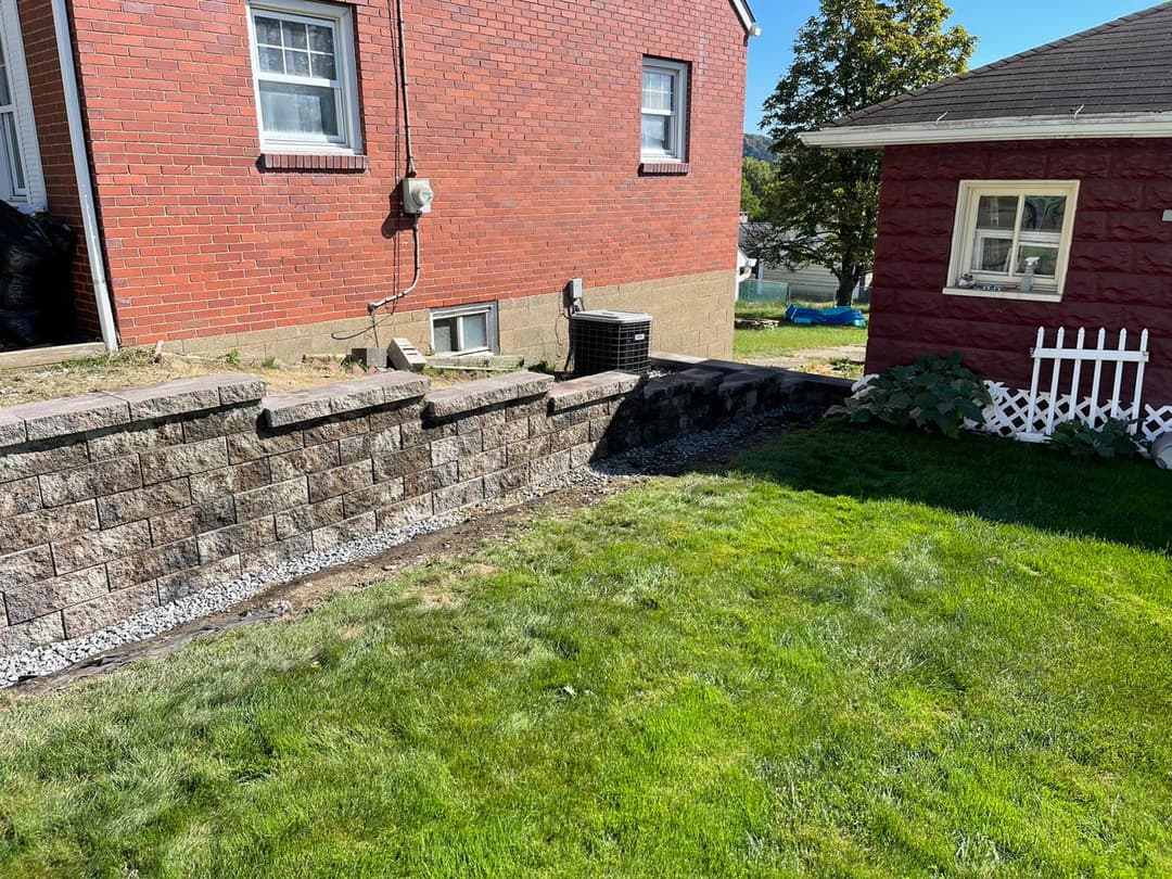 Landscaped backyard with a stone retaining wall, green grass, and two brick houses.