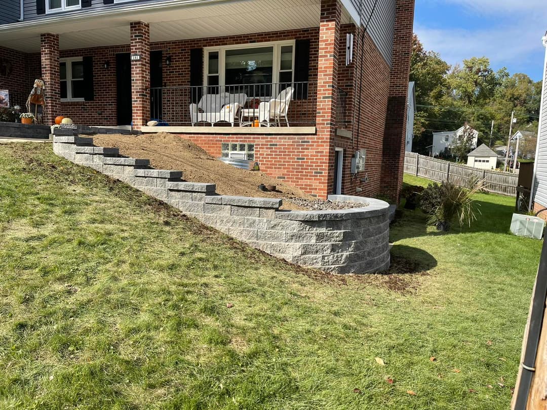 Landscape upgrade featuring retaining wall and freshly landscaped area next to a brick home.