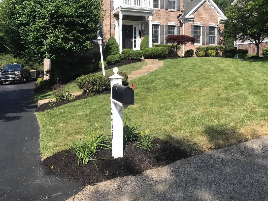 Black mailbox in front of a brick house with well-maintained lawn and landscaped garden.