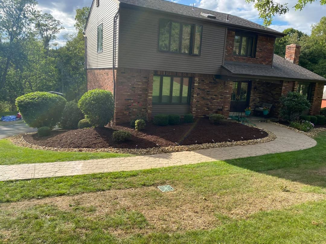Brick home with landscaped front yard, stone pathway, and lush greenery on a sunny day.