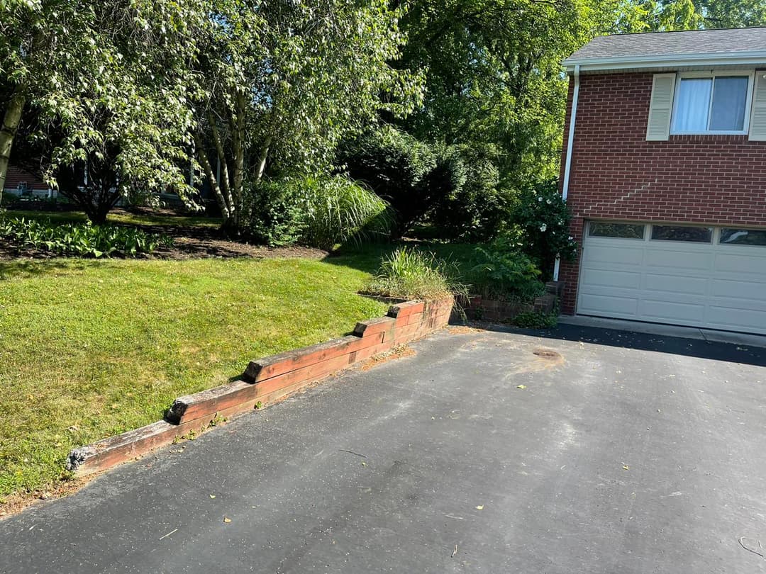 Brick wall landscaping beside a driveway and garage in a suburban home with greenery.