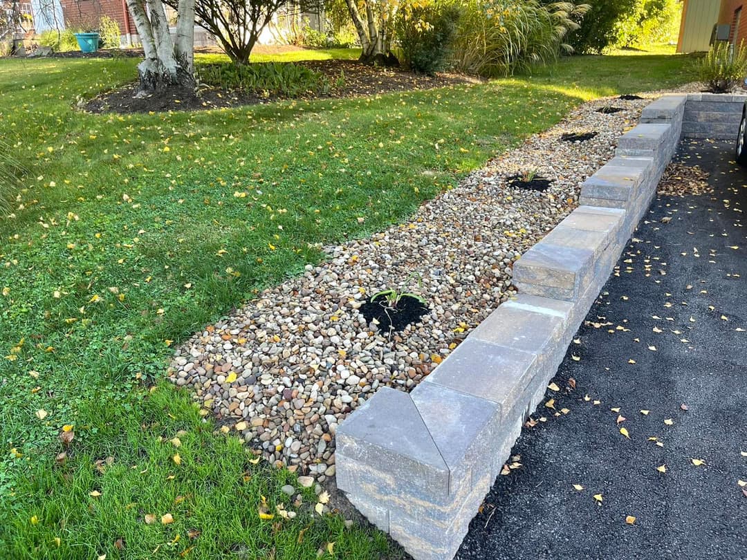 Landscaped yard with stone path, grass, and autumn leaves, featuring a retaining wall.