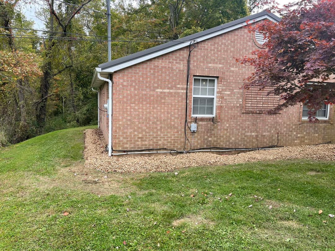 Side view of a brick building with gravel landscaping and trees in the background.