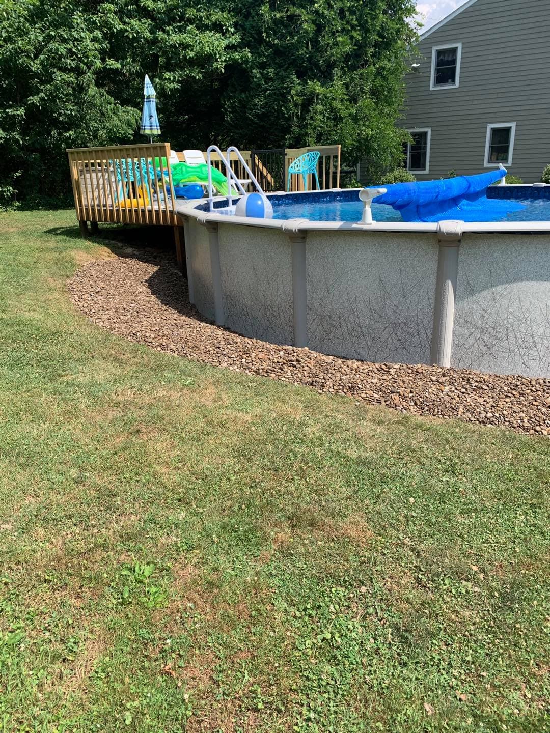 Above-ground pool with blue and green loungers, surrounded by gravel and grassy area.
