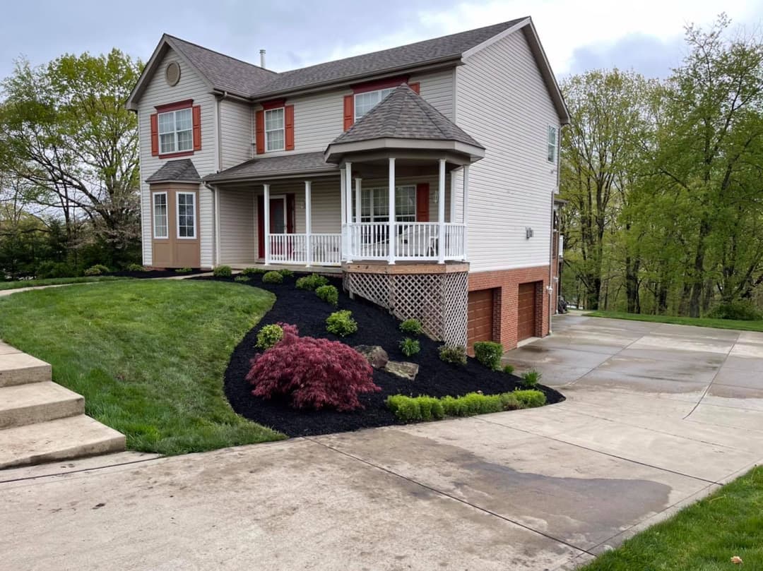 Modern two-story home with landscaped yard and driveway, featuring a porch and manicured garden.