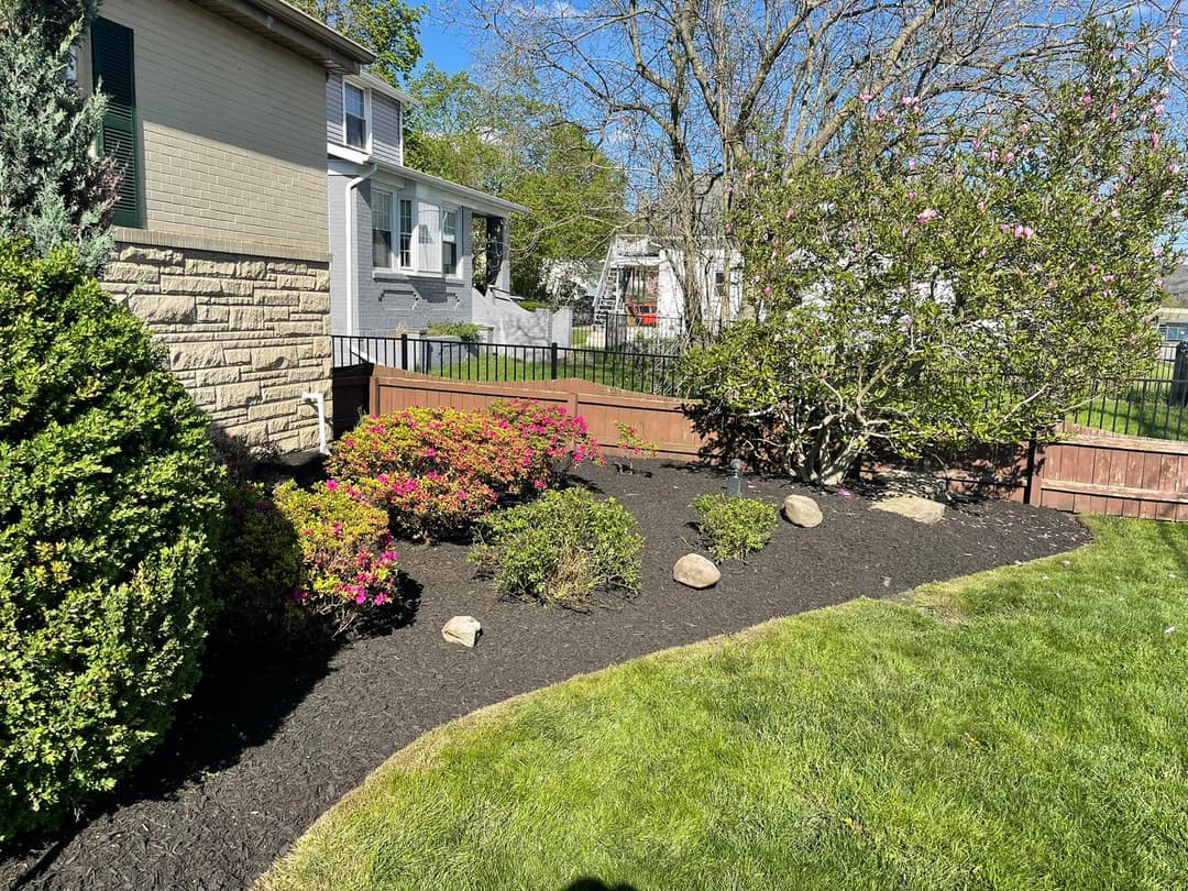 Colorful flowering shrubs and rocks in a landscaped yard with a home in the background.