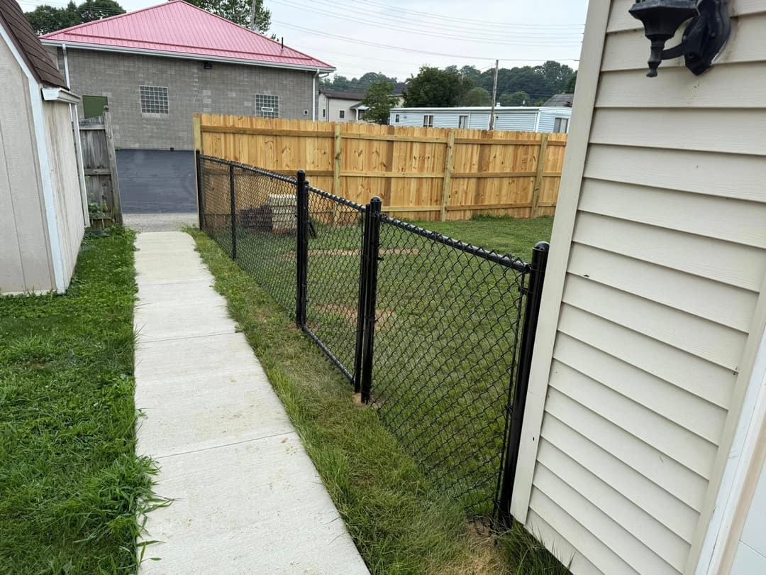 Pathway beside a chain link fence leading to a fenced yard and buildings in the background.