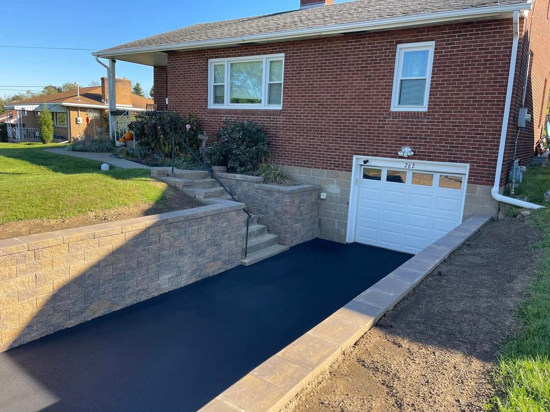 Residential exterior with brick house, landscaped yard, and newly paved driveway.