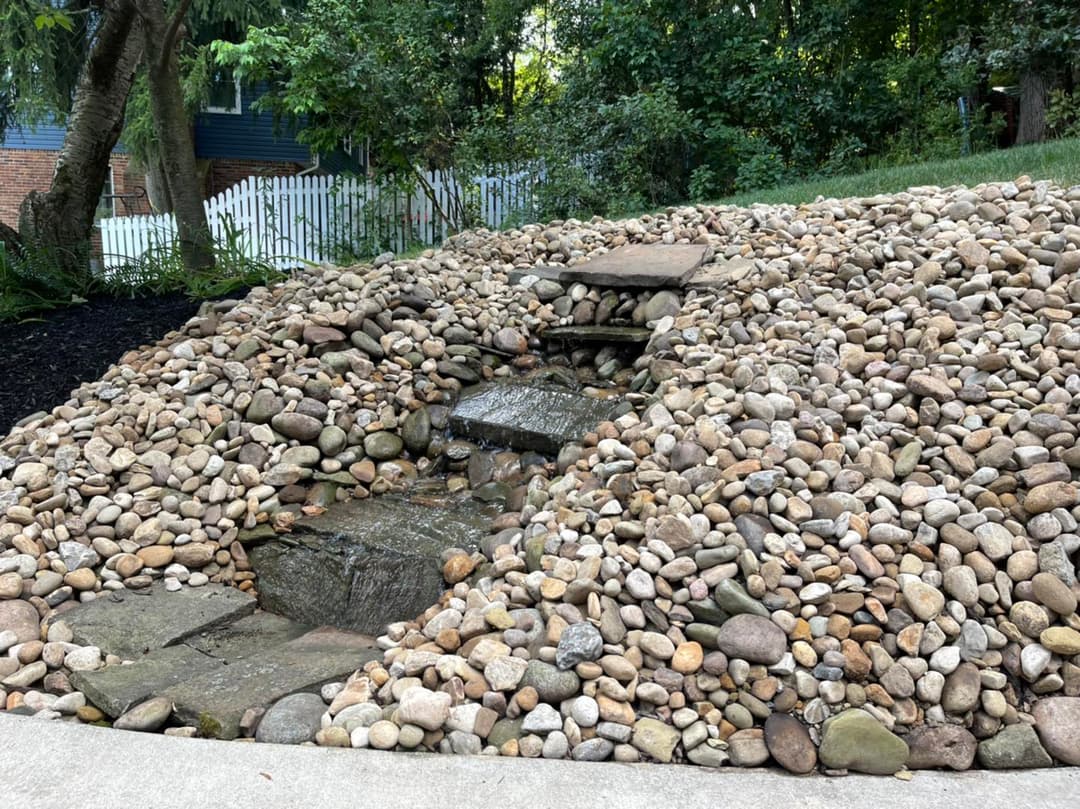 Water feature surrounded by smooth river stones in a landscaped garden setting.