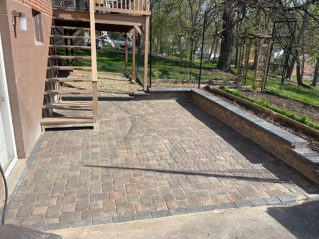 Paved outdoor patio with stone bricks and wooden stairs, surrounded by green landscape.