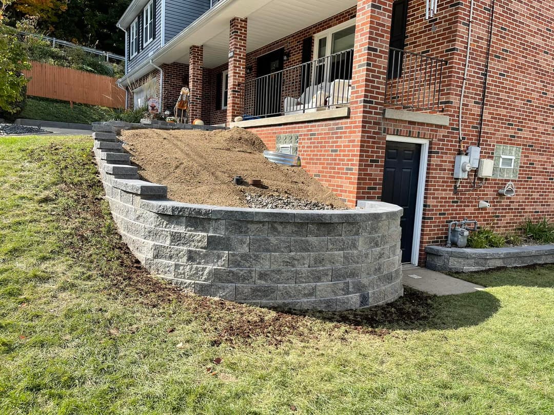 Landscaped yard featuring a stone retaining wall and soil ready for planting near a brick home.