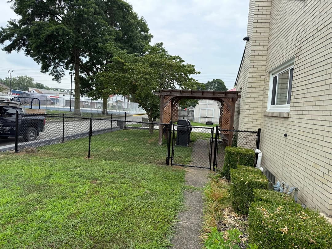 View of a fenced yard with a gazebo and trash can beside a brick building.