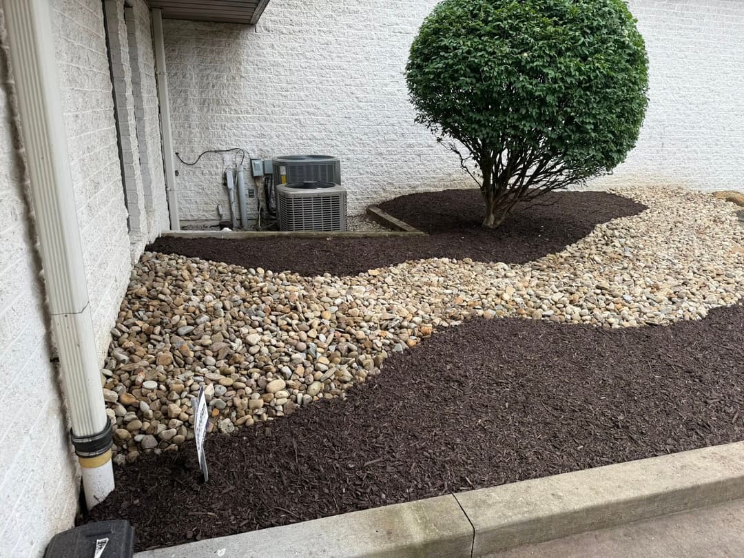 Landscaped area with a rock bed, mulch, and a bush near an air conditioning unit.