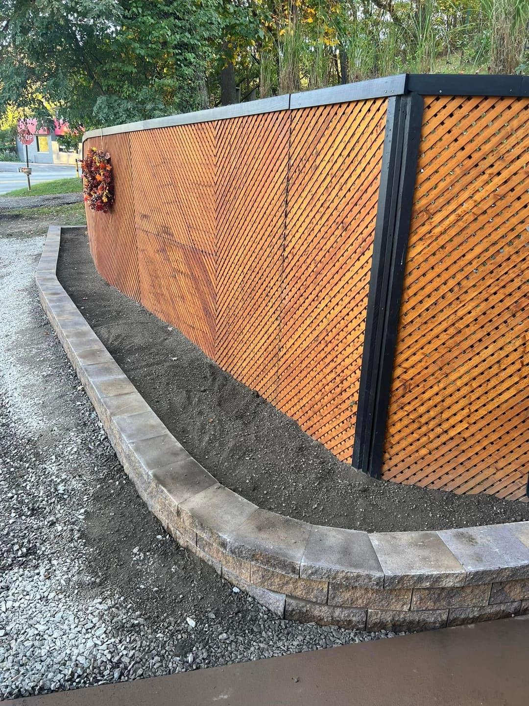 Decorative wooden fence with curved stone border and freshly prepared soil for planting.