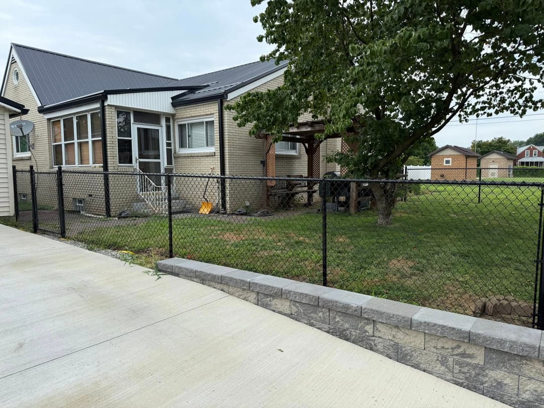 Modern residential home with a fenced yard and trees, featuring a concrete driveway.