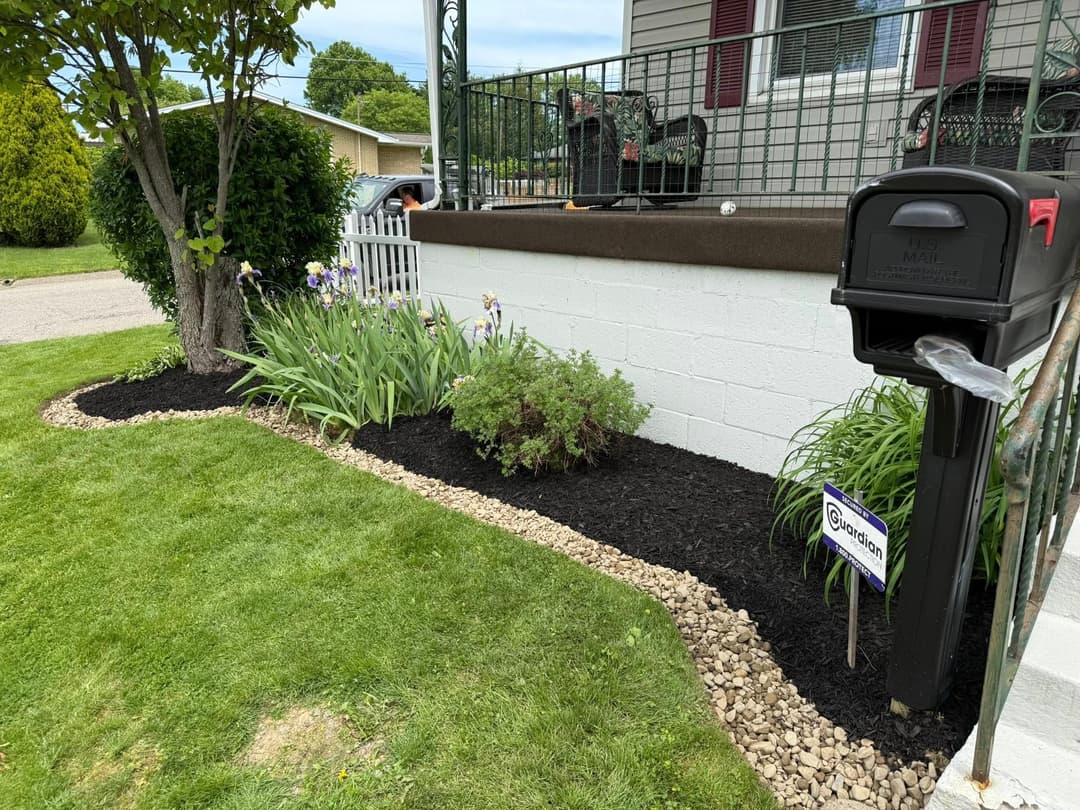 Mailbox in a front yard with landscaped flower beds and freshly laid mulch. Green lawn visible.