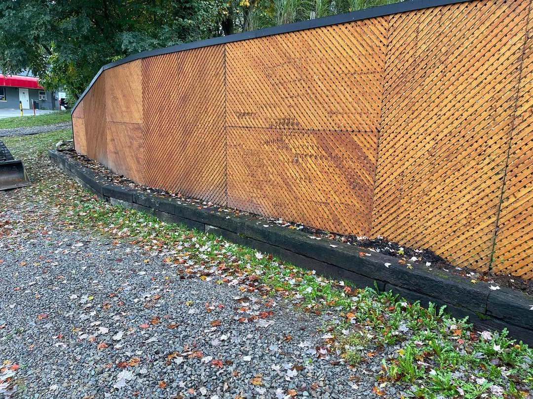 Wooden fence with a textured pattern, surrounded by gravel and autumn leaves.
