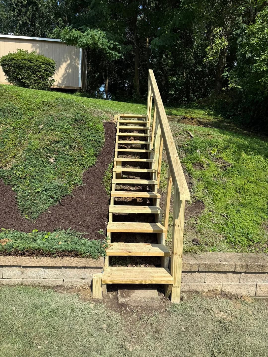 Wooden backyard stairs leading up a hillside with green landscaping and mulch.