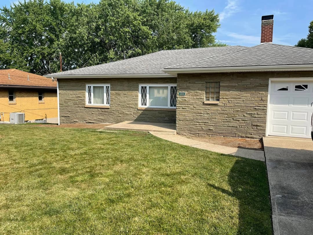 Single-story home with stone exterior, green lawn, and driveway on a sunny day.