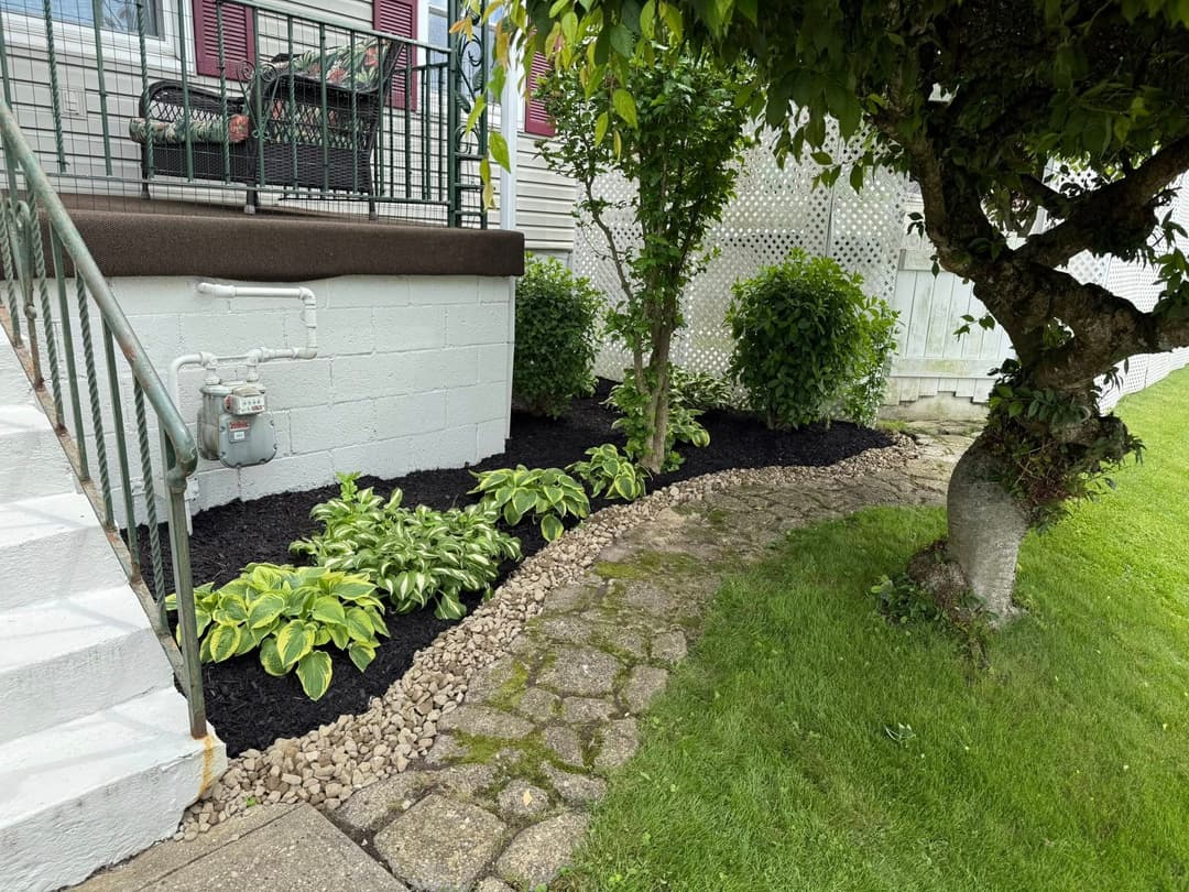 Lush garden with hostas, stone path, and manicured shrubs beside a home entrance.