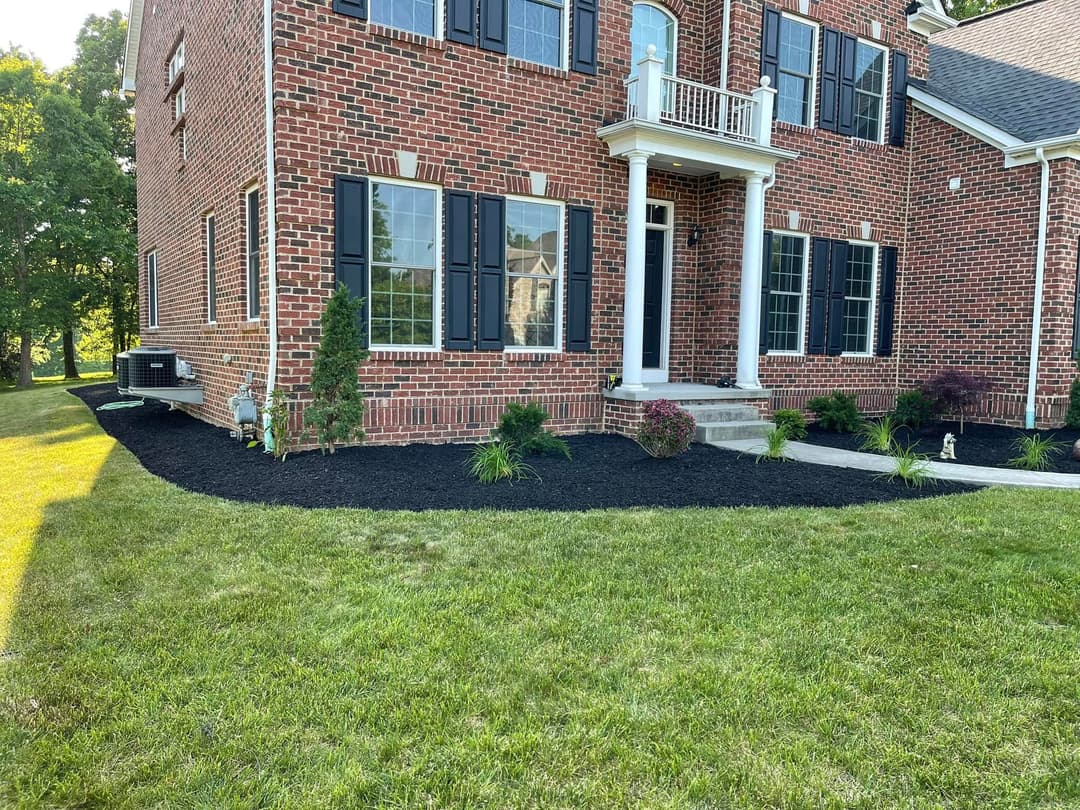 Front view of a brick house with landscaped lawn and shrubs, featuring a porch and black shutters.