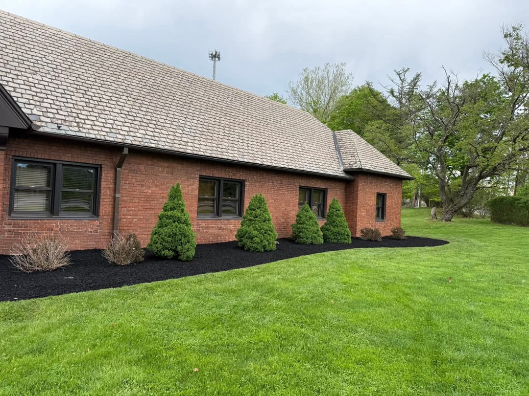 Brick building with a sloped roof, manicured lawn, and neatly trimmed shrubs along the foundation.