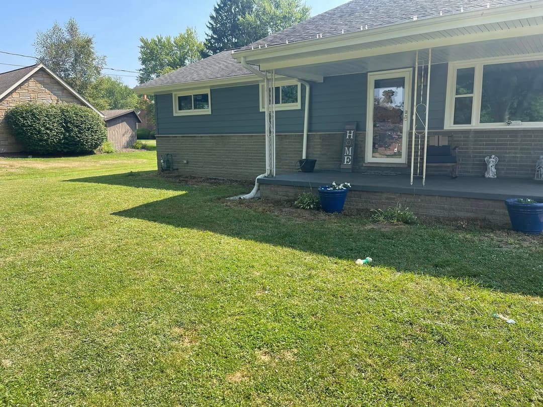Cozy home exterior with green lawn, porch, and potted plants in sunny neighborhood setting.