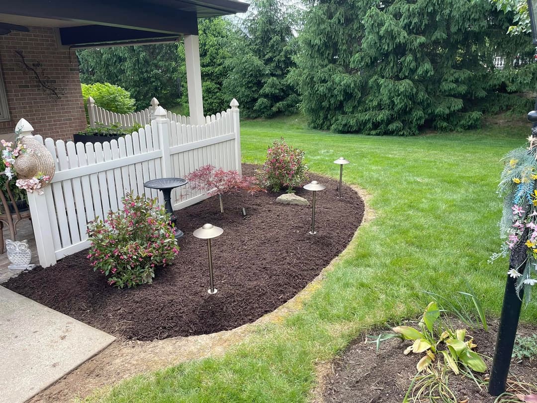 Landscape design featuring flower beds, solar lights, and a white picket fence in a lush garden.