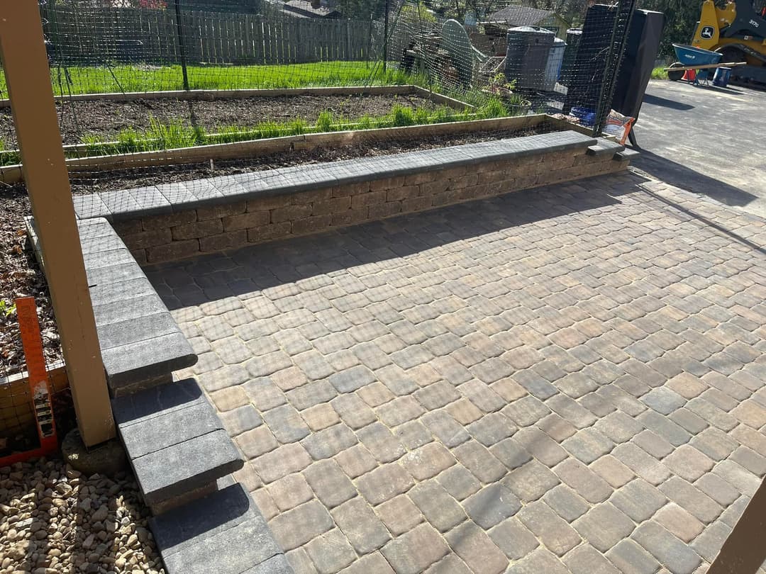 Paved outdoor patio with stone seating wall and landscaped yard in background.