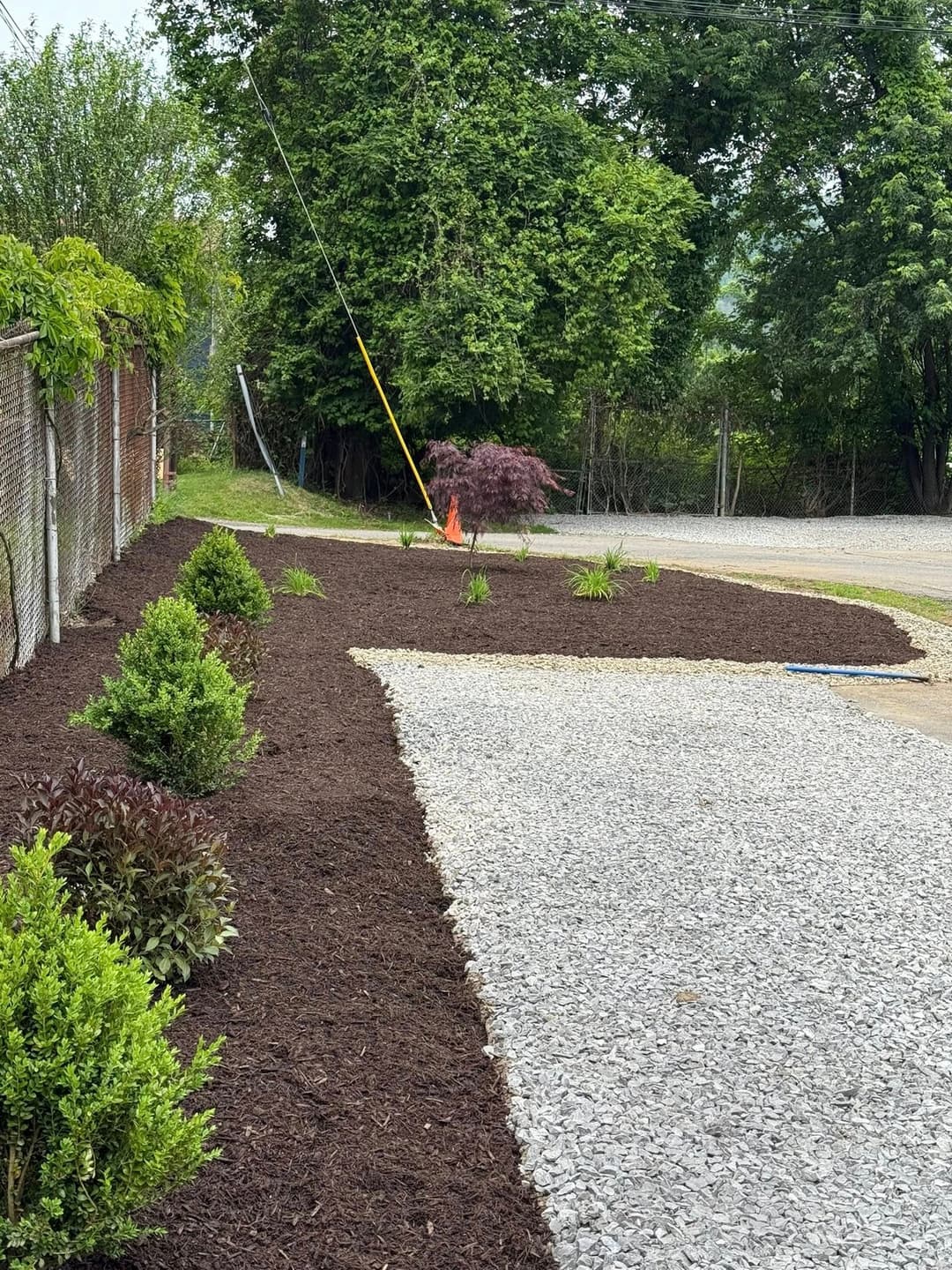 Landscaped garden area with fresh mulch, plants, and gravel pathway beside a fence.