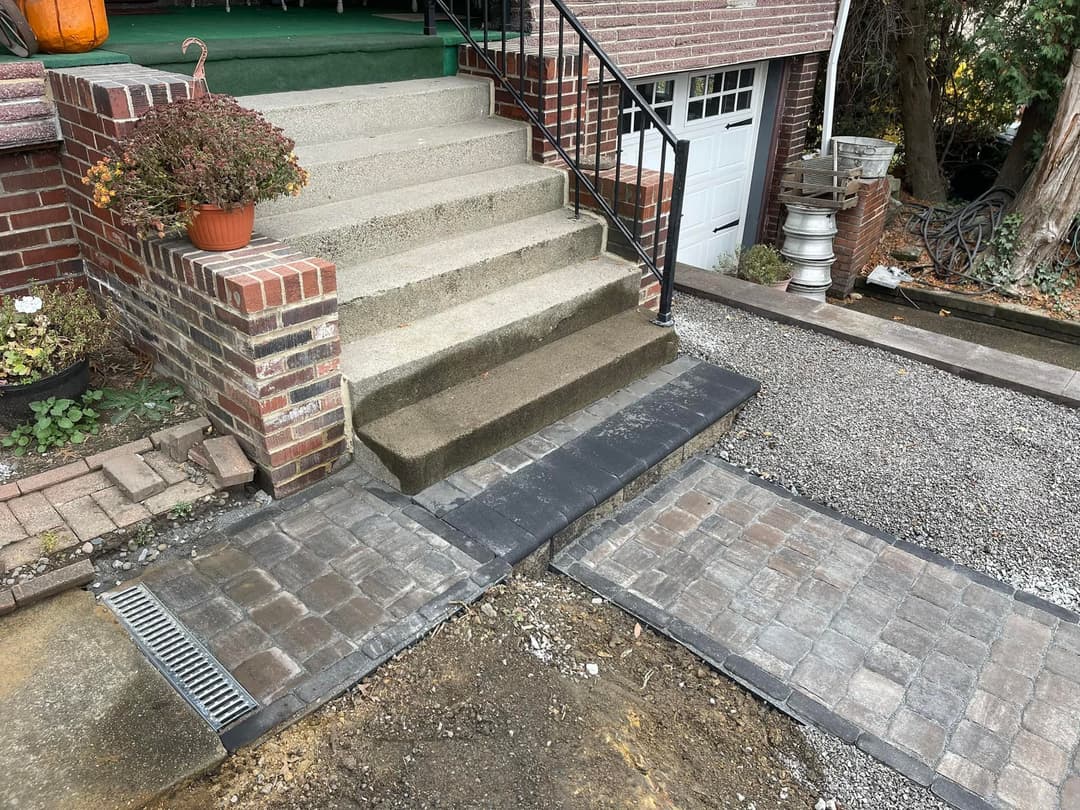 Concrete steps leading to a home with a cobblestone pathway, surrounded by landscaping.