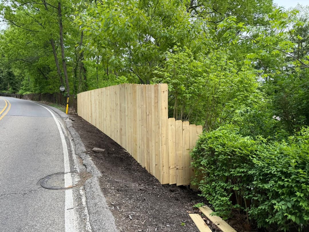 New wooden fence along a road, surrounded by greenery and trees.