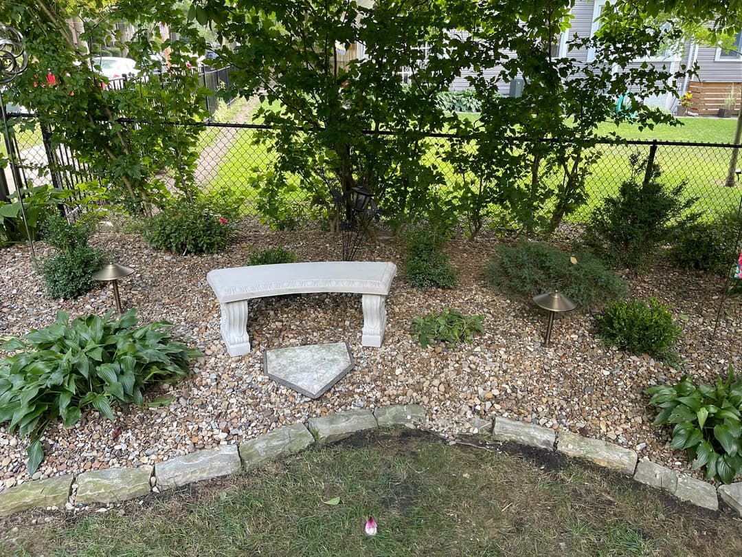 Garden scene with a stone bench surrounded by plants and decorative lights on gravel.