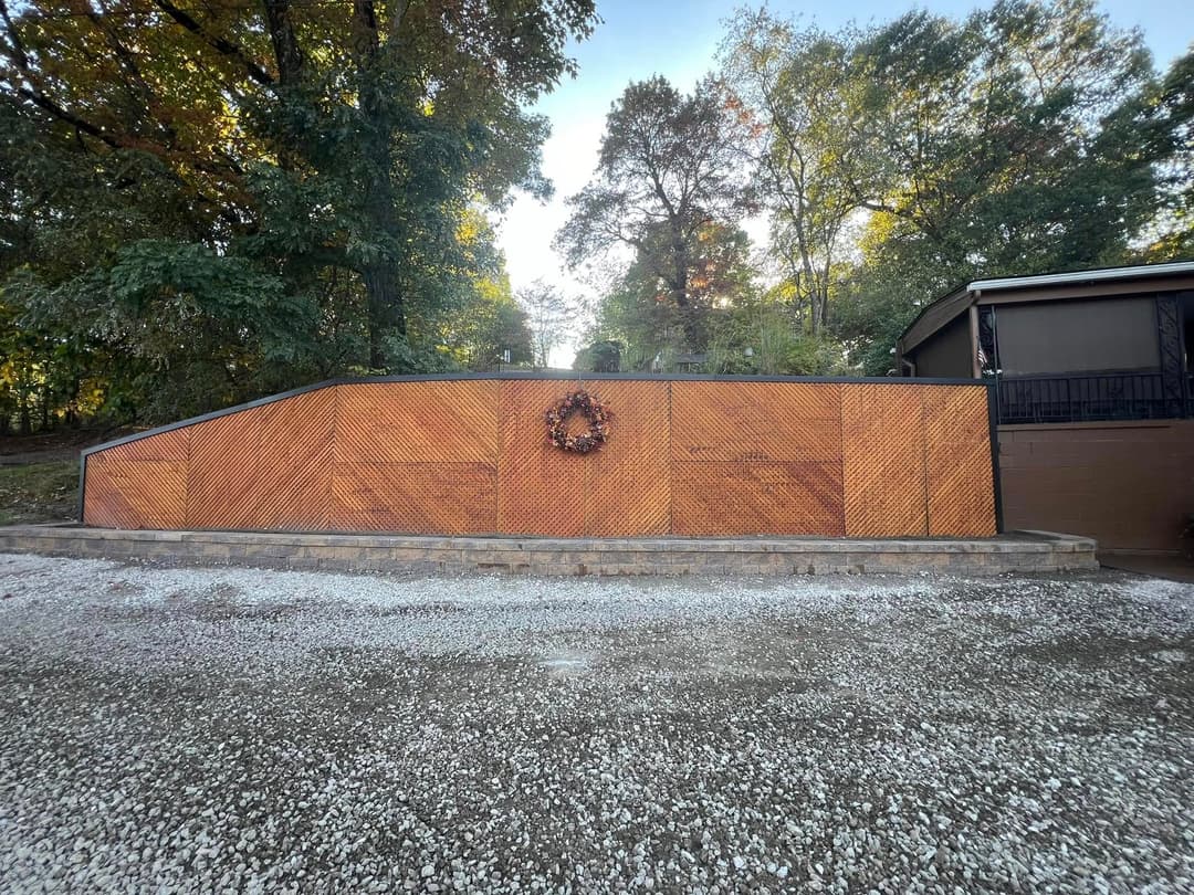 Wooden wall with geometric pattern, surrounded by trees, featuring a decorative wreath.