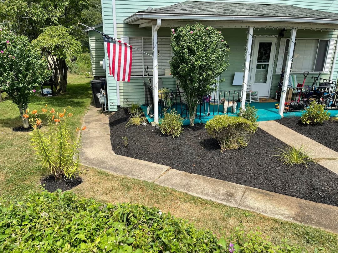 Front yard with colorful flowers, neatly landscaped shrubs, and an American flag hanging.