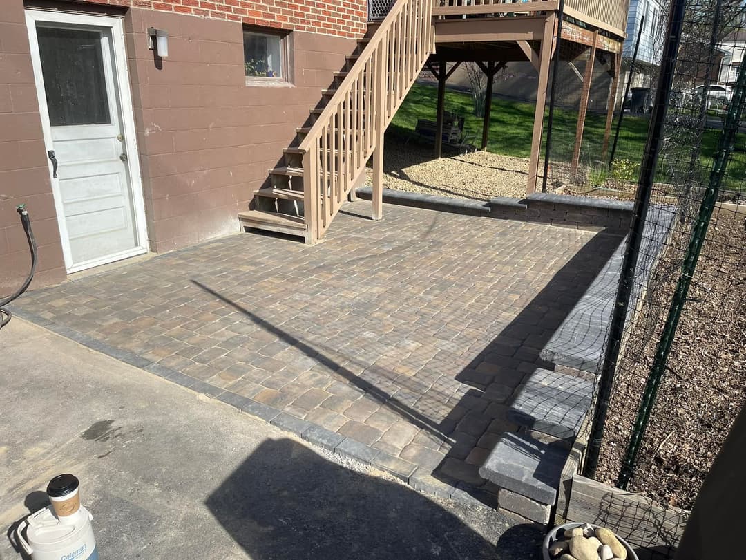 Paved outdoor patio area with steps and landscaping, featuring brick pattern and fence.